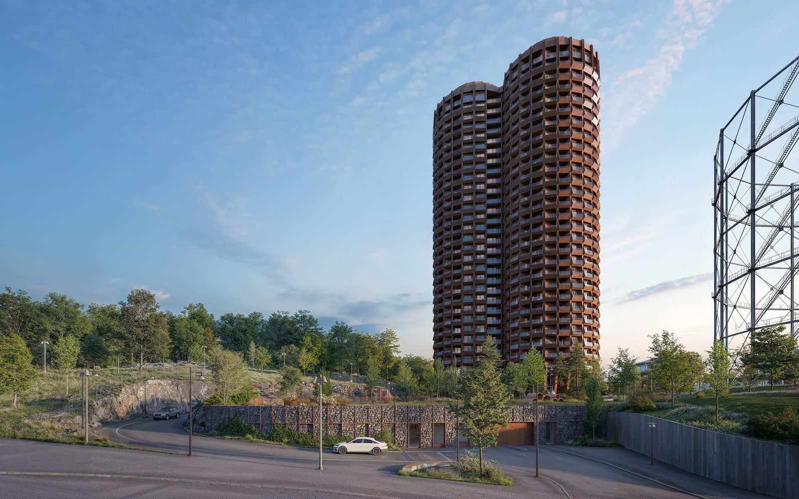 Stadsljus: two joined round towers in brick red, seen from Gasverksvägen with the gasholder’s steel frame to the right